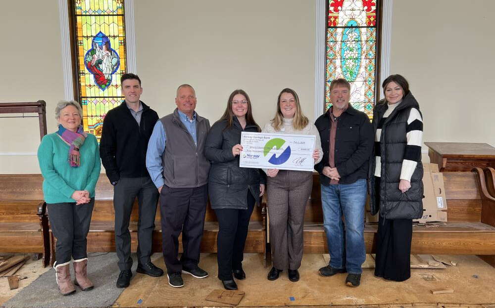 Seven people stand in a church and hold an oversize check.