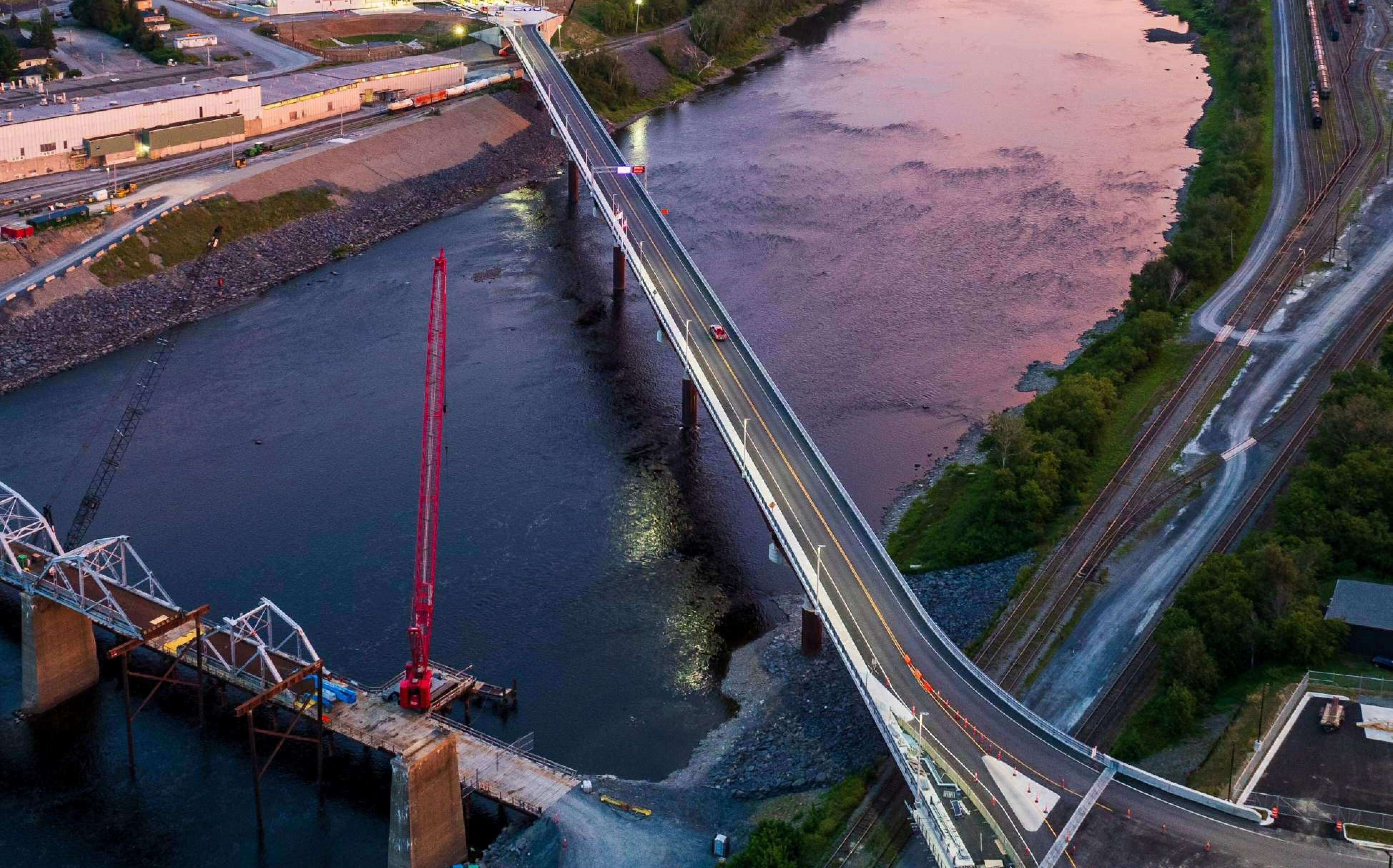 An aerial view of a bridge over a river in the pink sunlight.