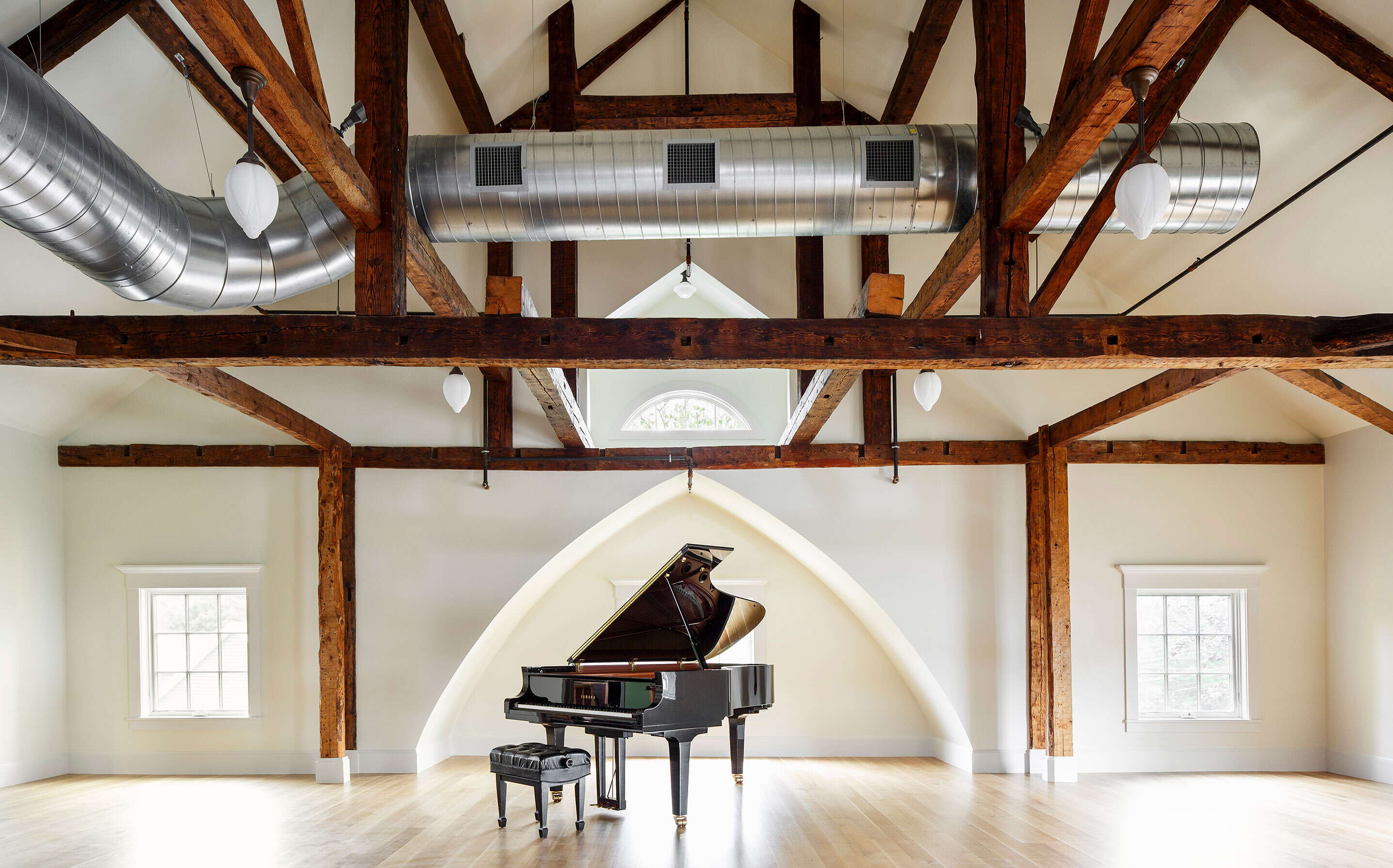 A performance hall has big ductwork at the ceiling and a grand piano.