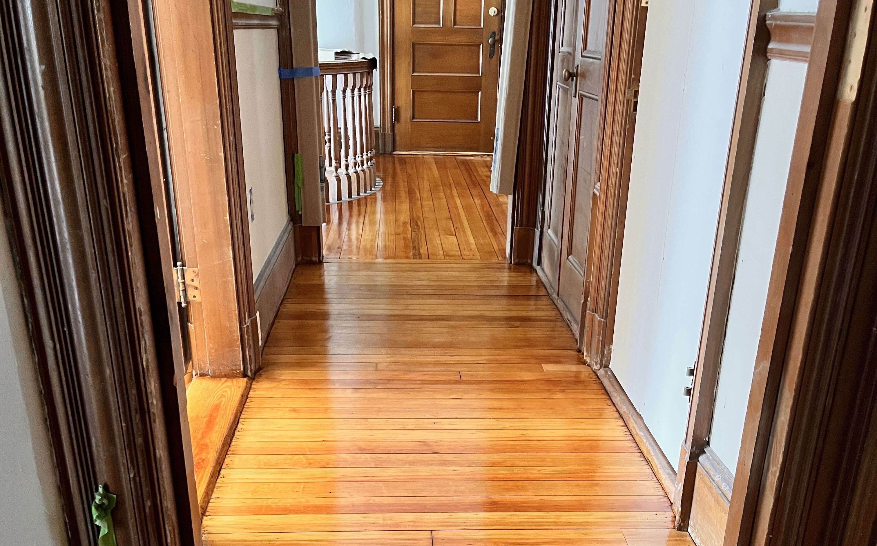 A wood floored-hallway leads to a door.