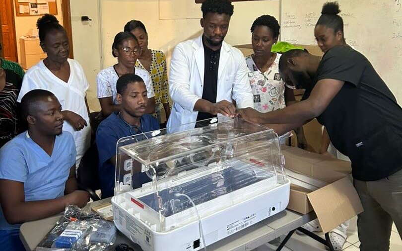 People look on as a person works on a machine.