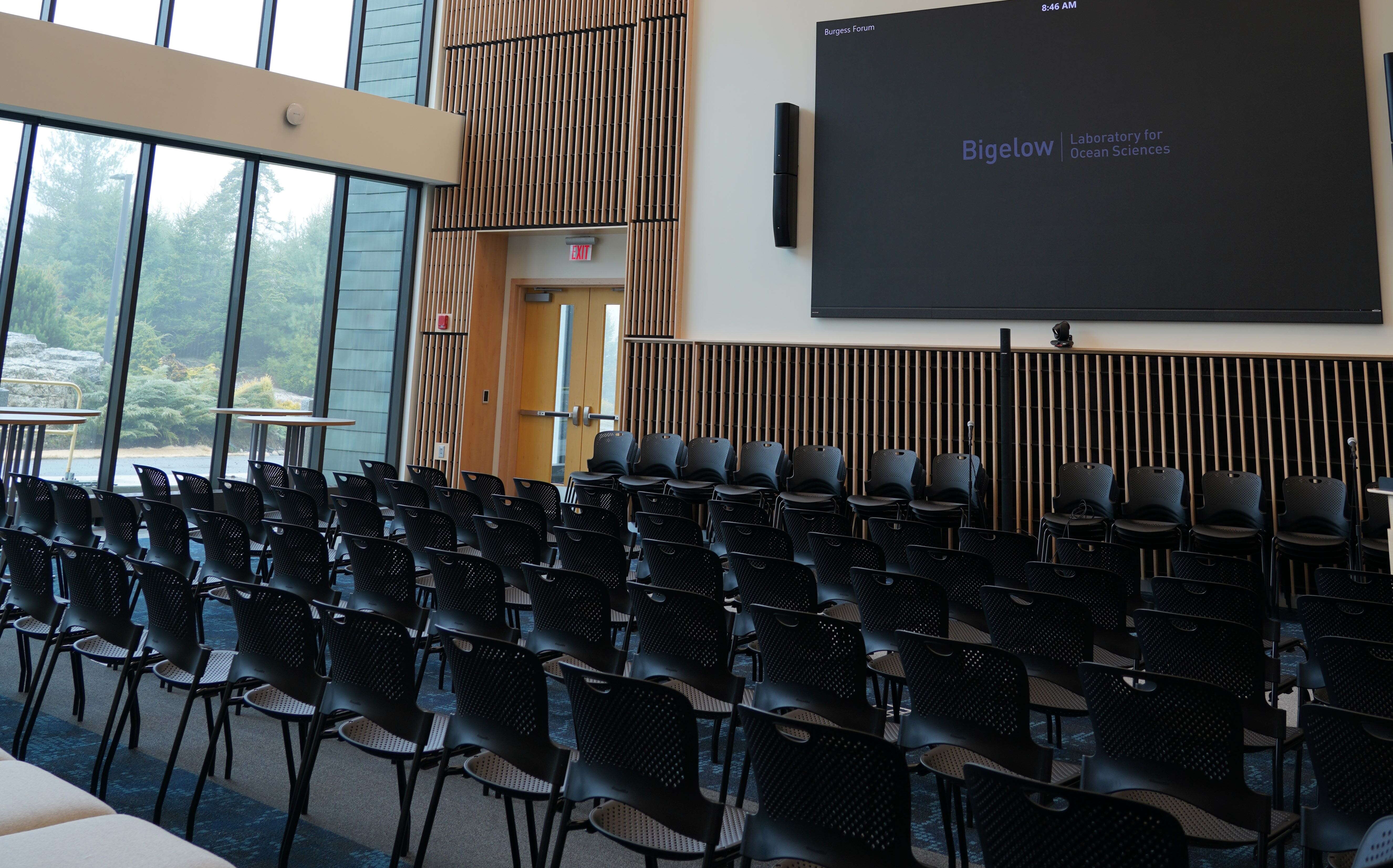 A room has a big screen and lots of chairs in rows.