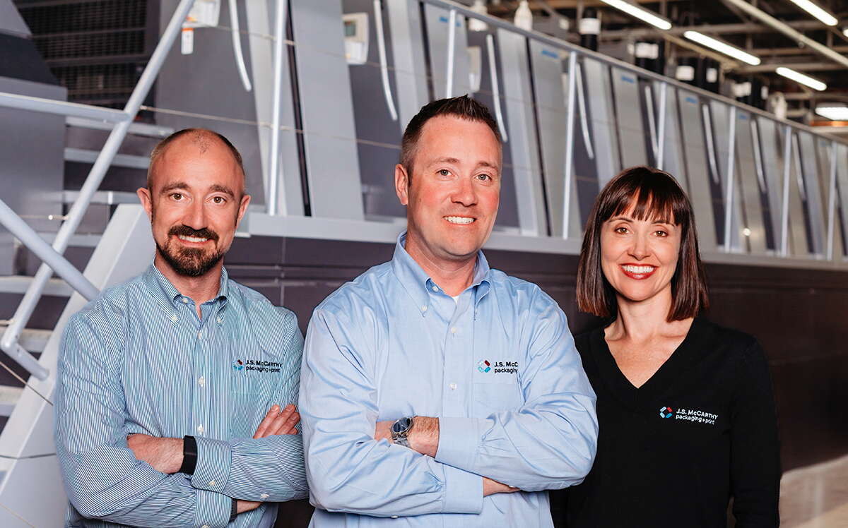 Three people in front of industrial machinery.