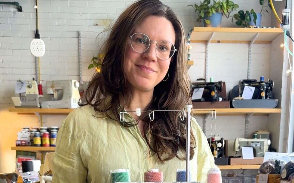 A person stands with a sewing machine.