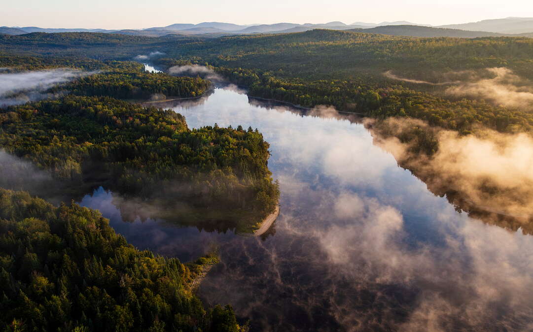 An aerial view shows a river and woods.
