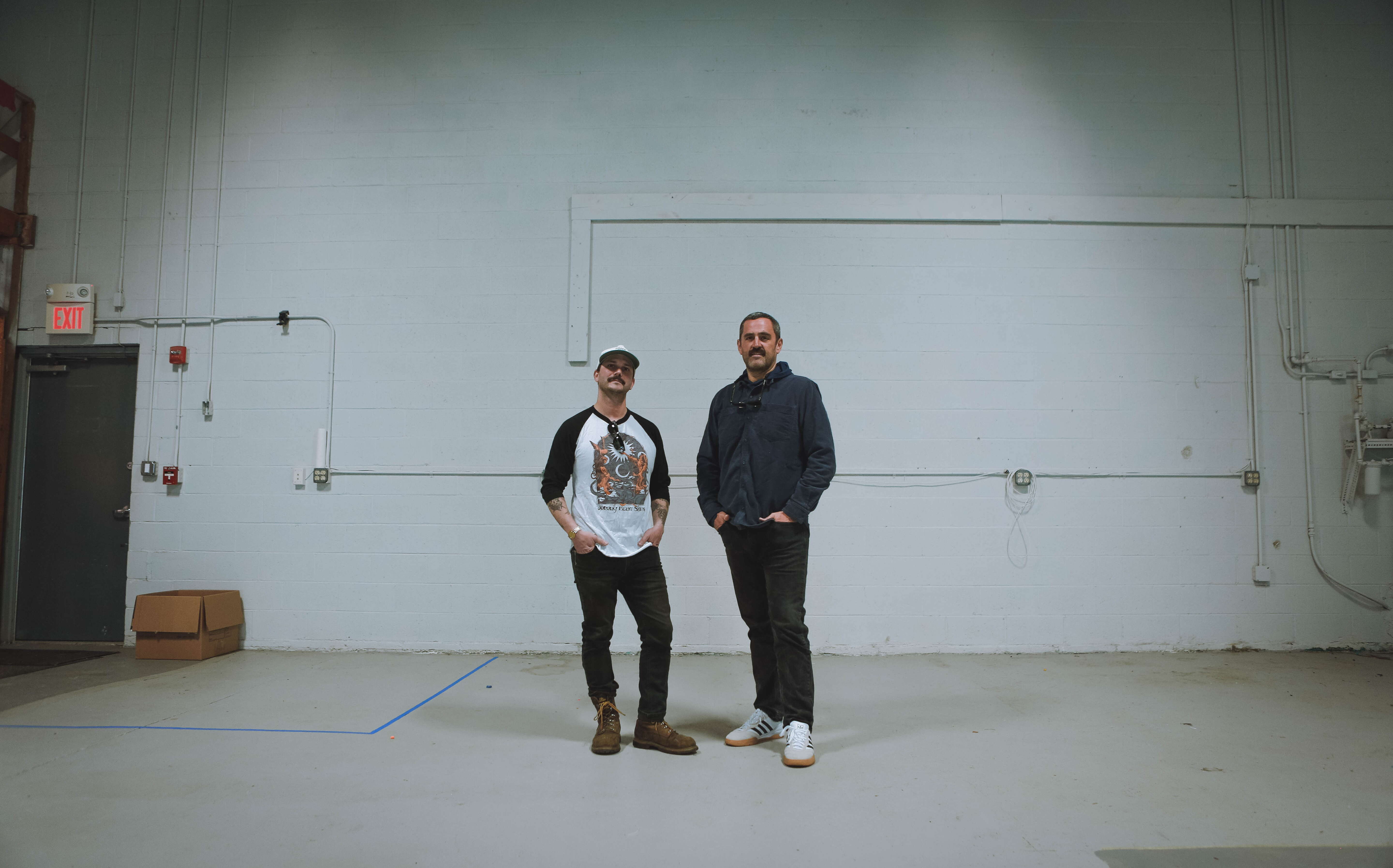 Two people stand inside an empty space.