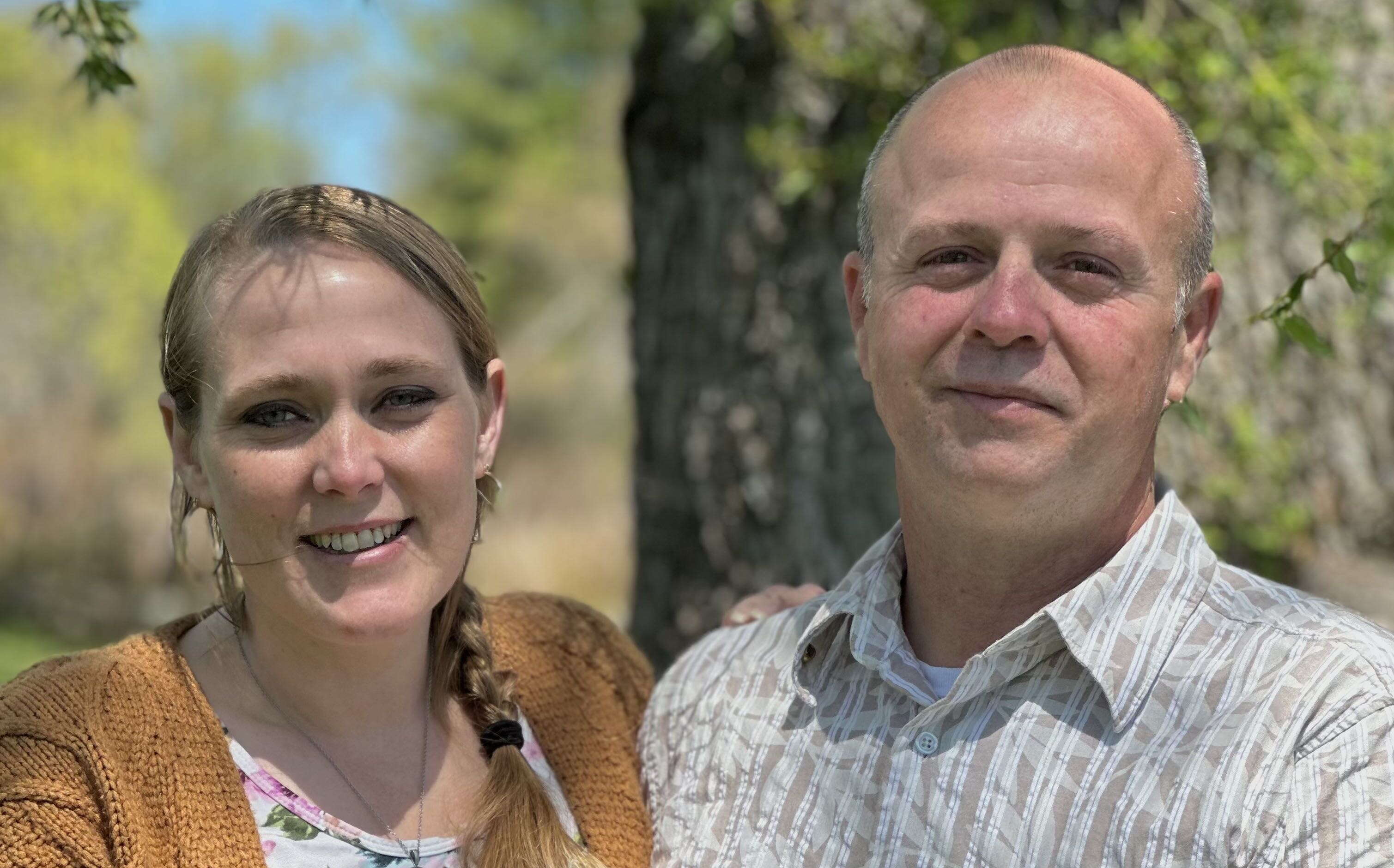 Two people pose near a tree.