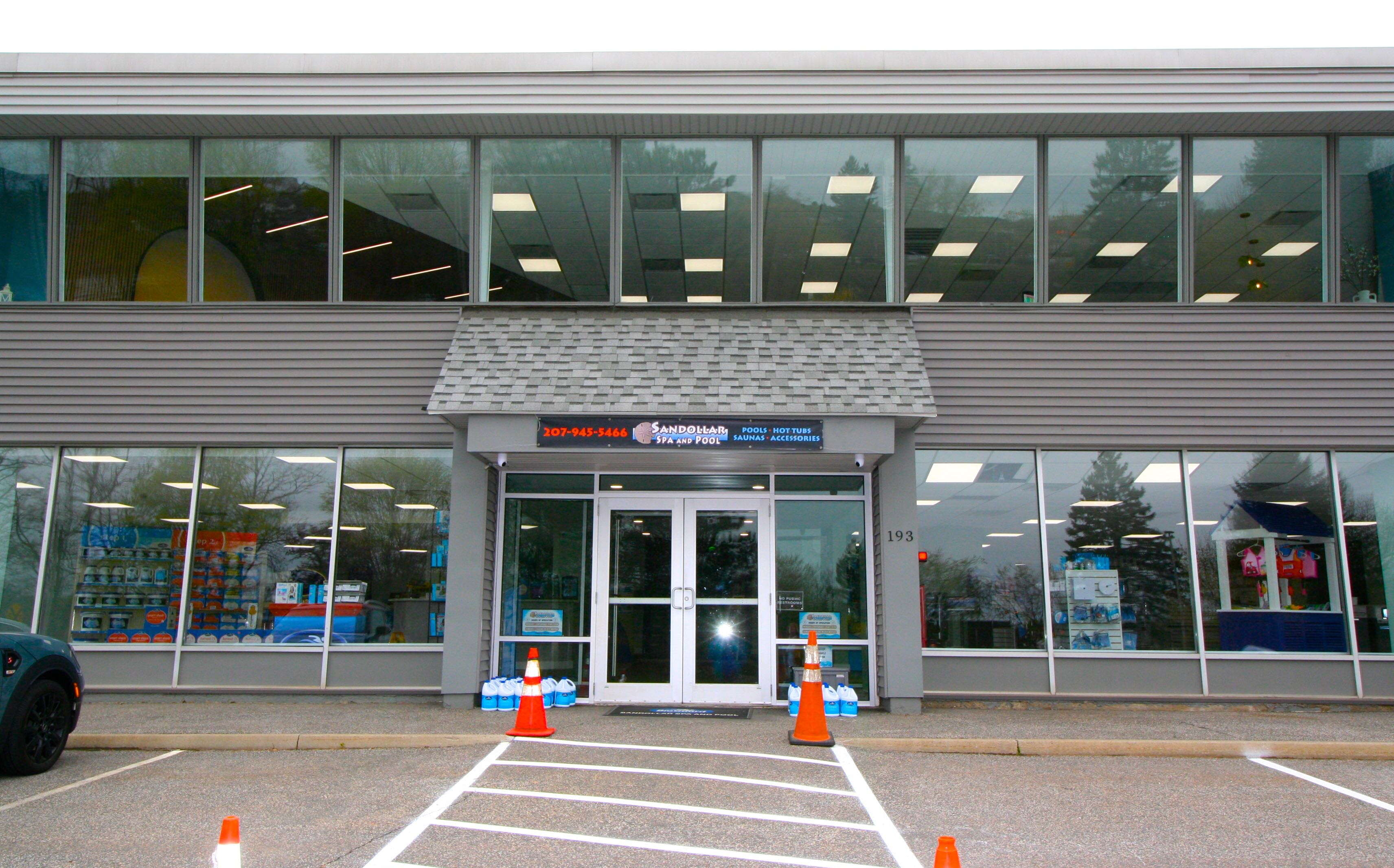 The exterior of a building has big windows and traffic cones.