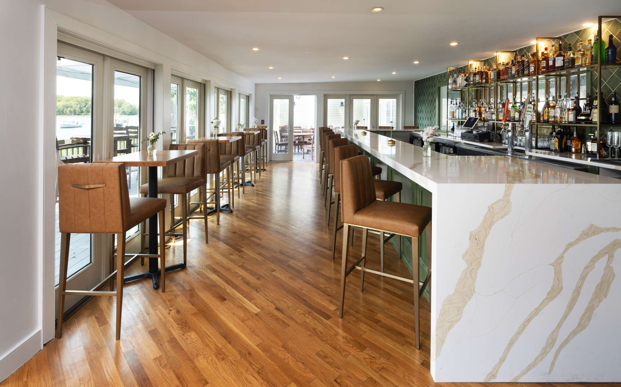 A room has stools, high tables and a counter with a wood floor.