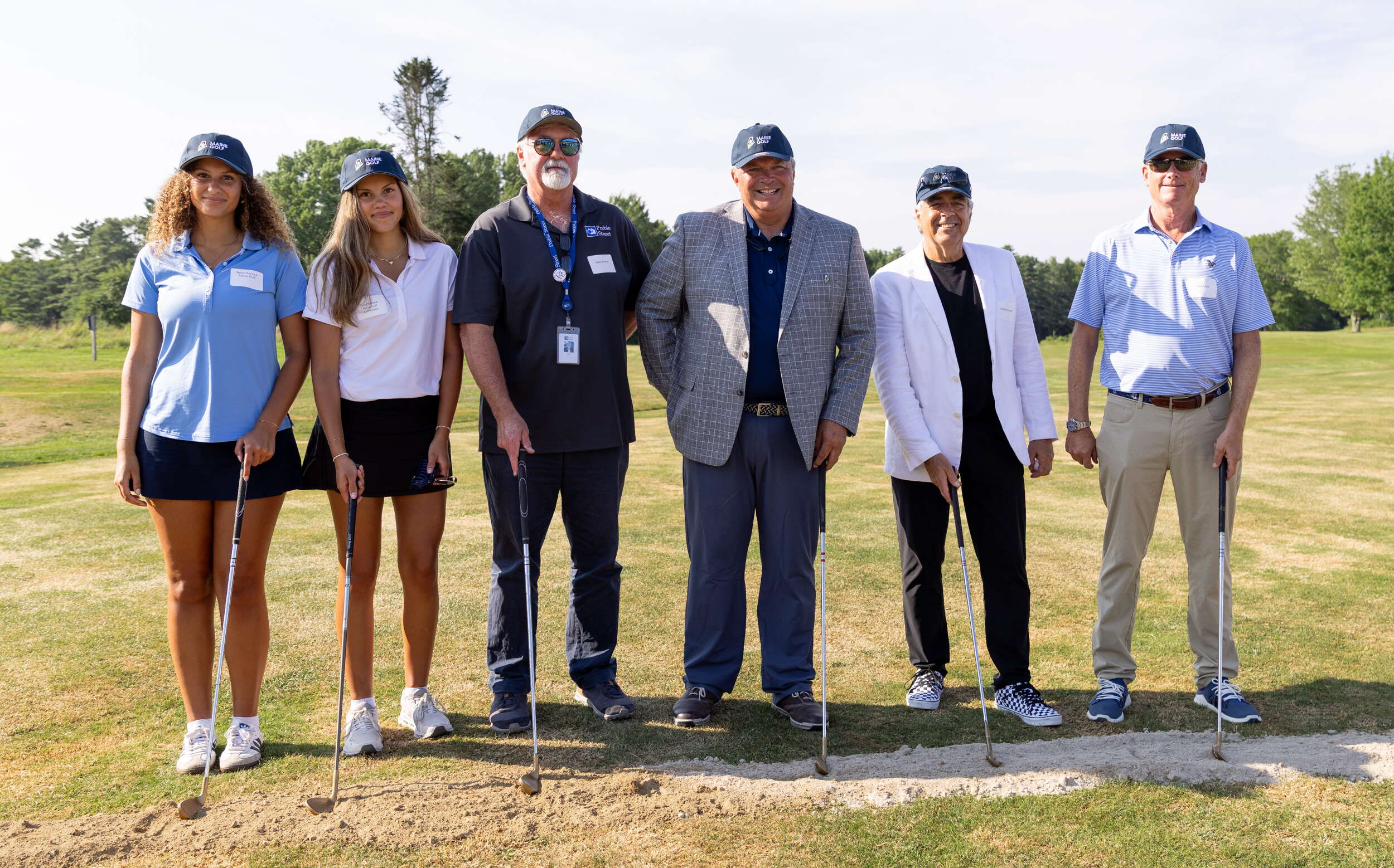 Six people pose in a line with golf clubs.