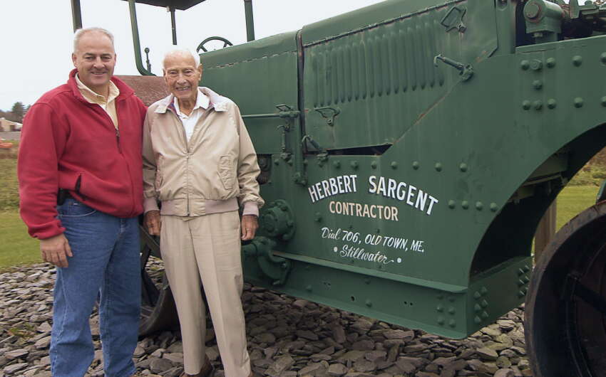 Two people stand outside next to a green vehicle.