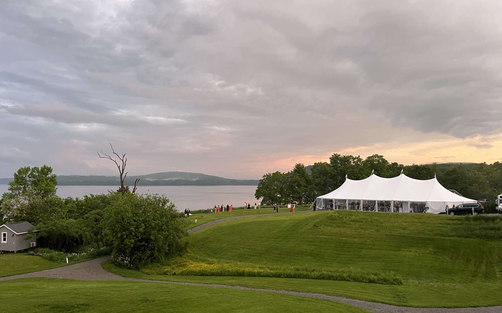 A white tent sits near the water in a field.