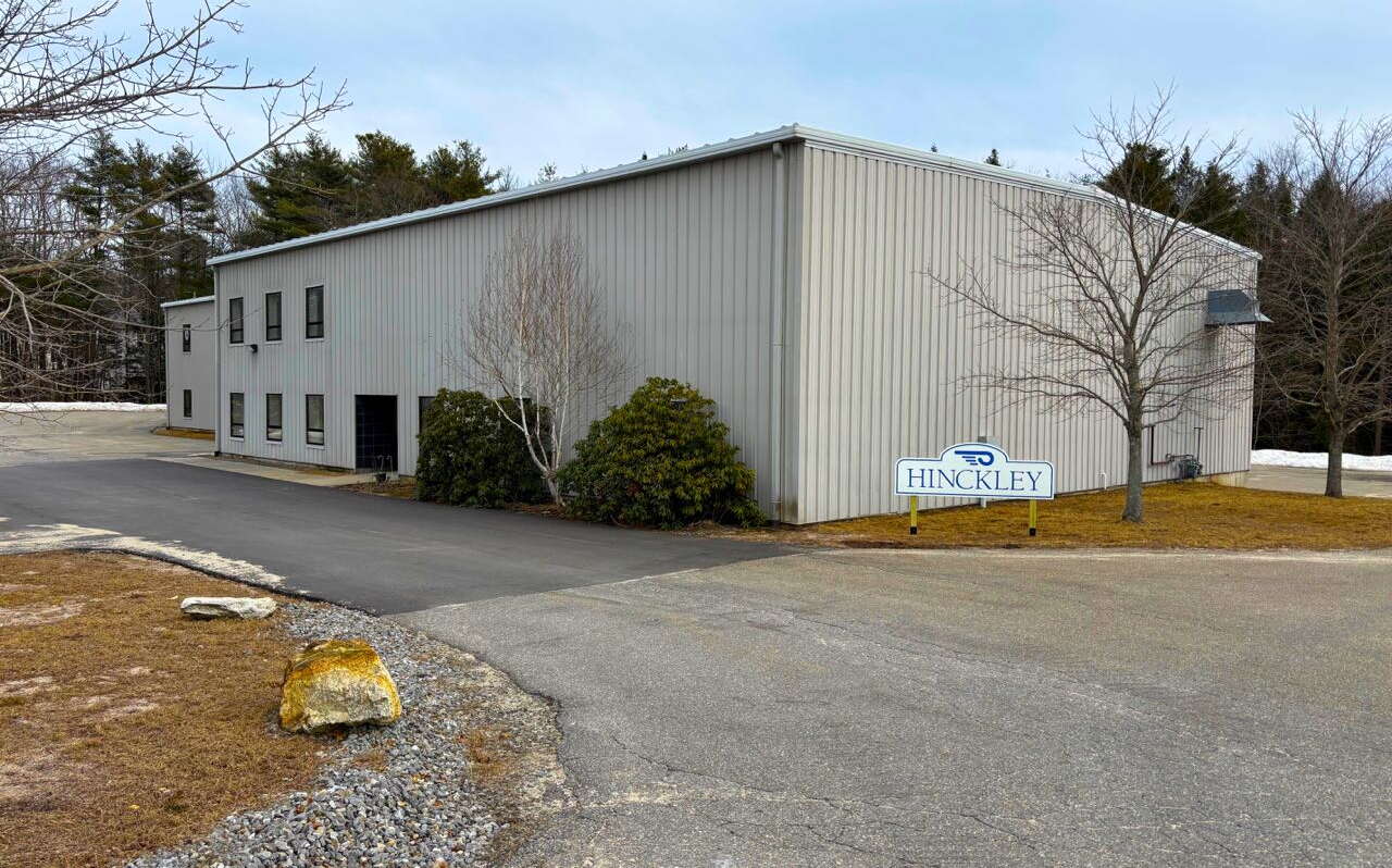 A tan building has a sign and driveway out front.