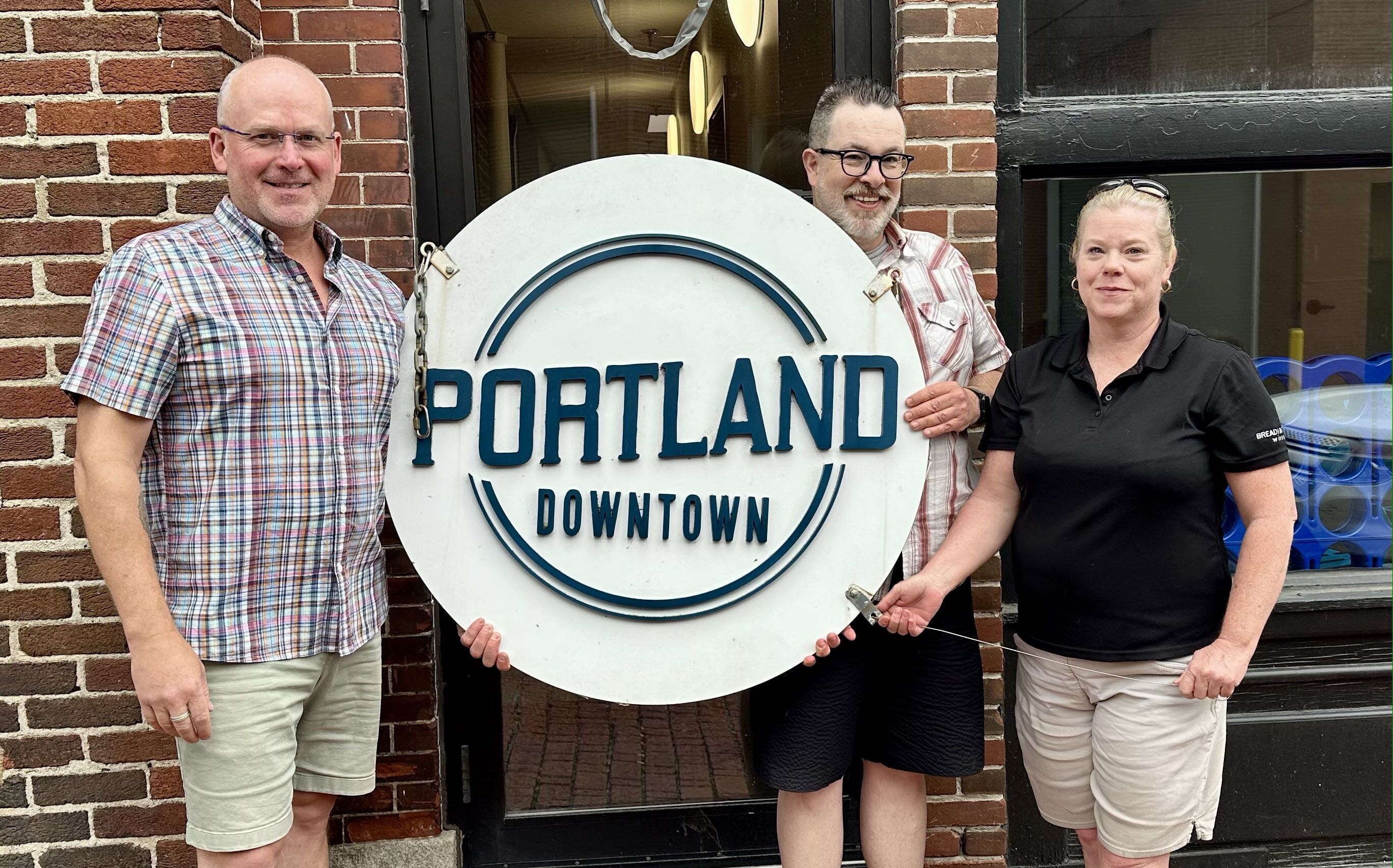 Three people pose with a circular sign.