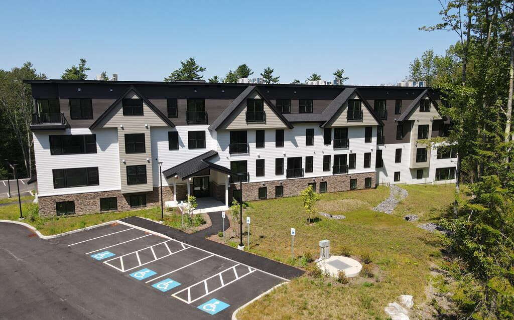An aerial photos shows a building with white siding and a lawn and parking lot.