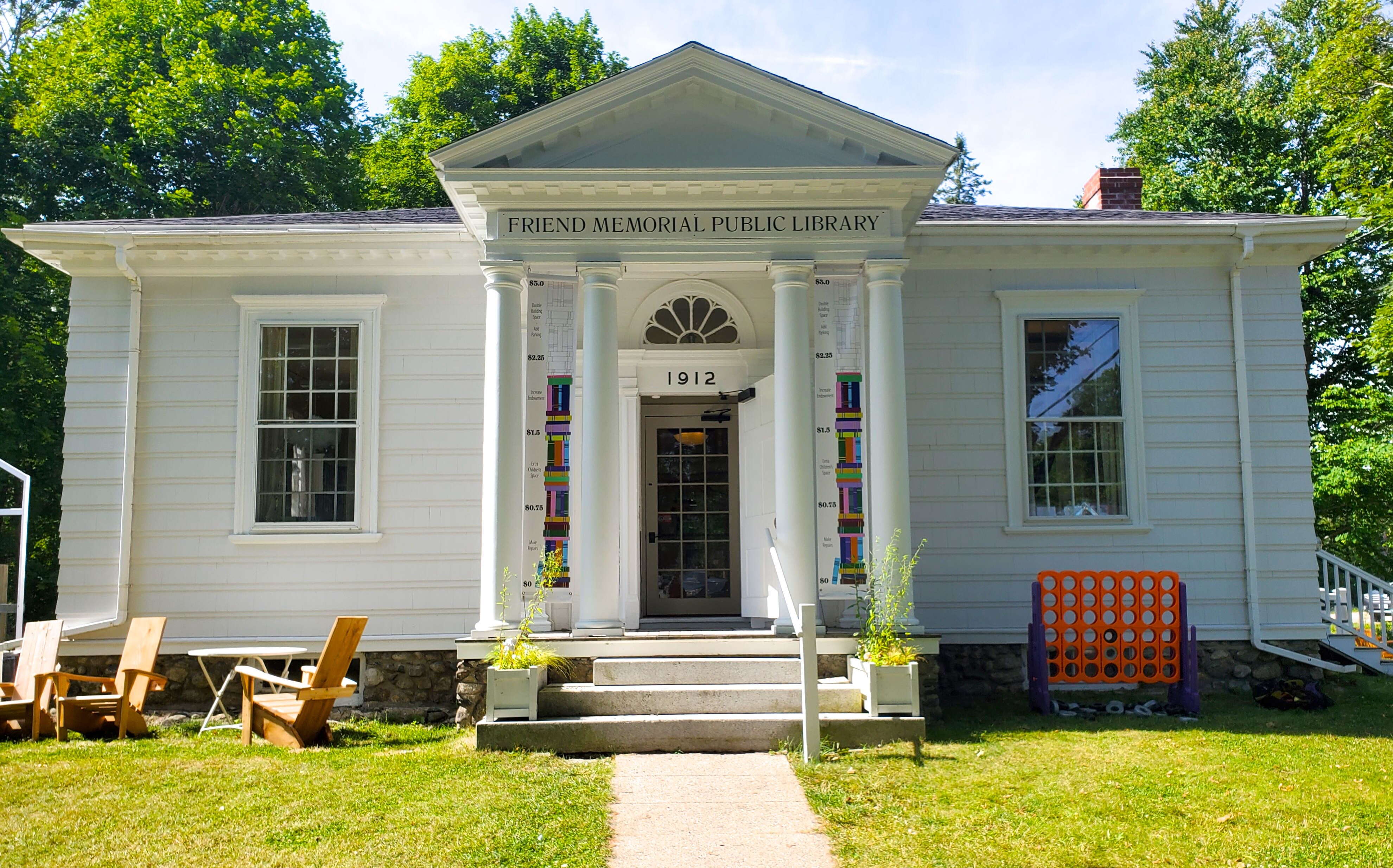 The exteiror of a bulding has white siding and a lawn and path.