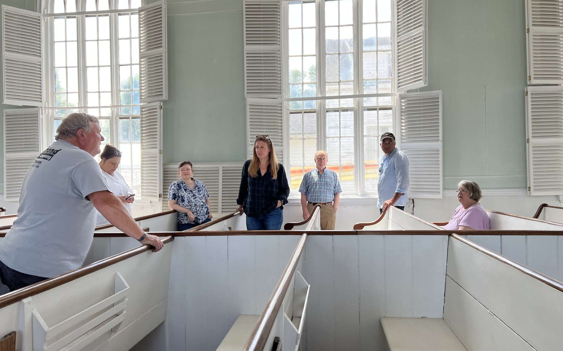 People stand among white-painted pews.