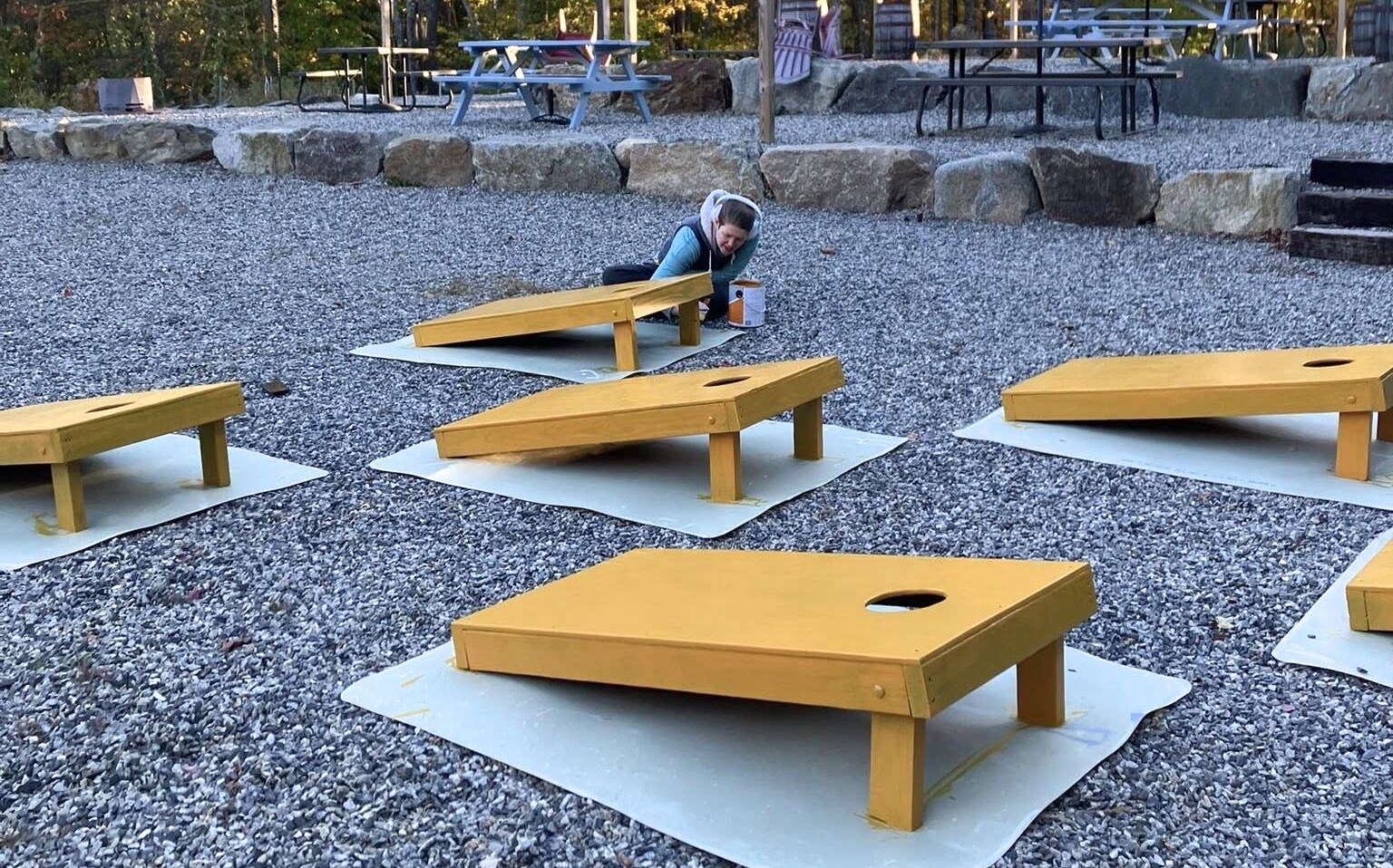 A person paints wooden objects outside.
