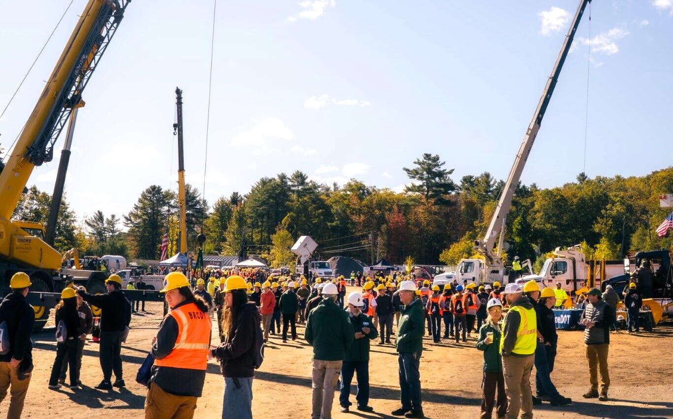 A crowd of people stand near some cranes.