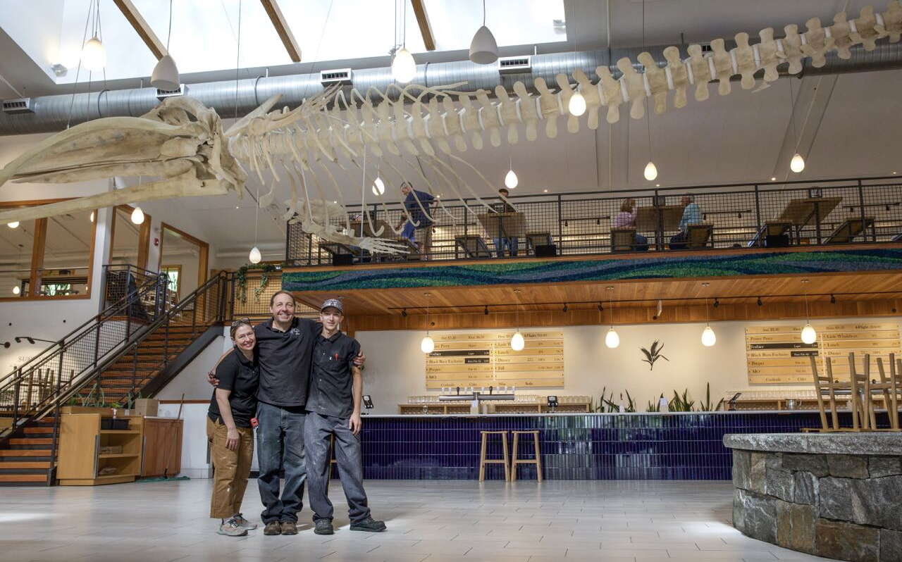 Three people stand below a skeleton.