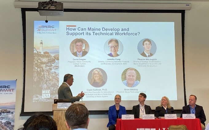 A person stands at a lectern and others sit at a table.