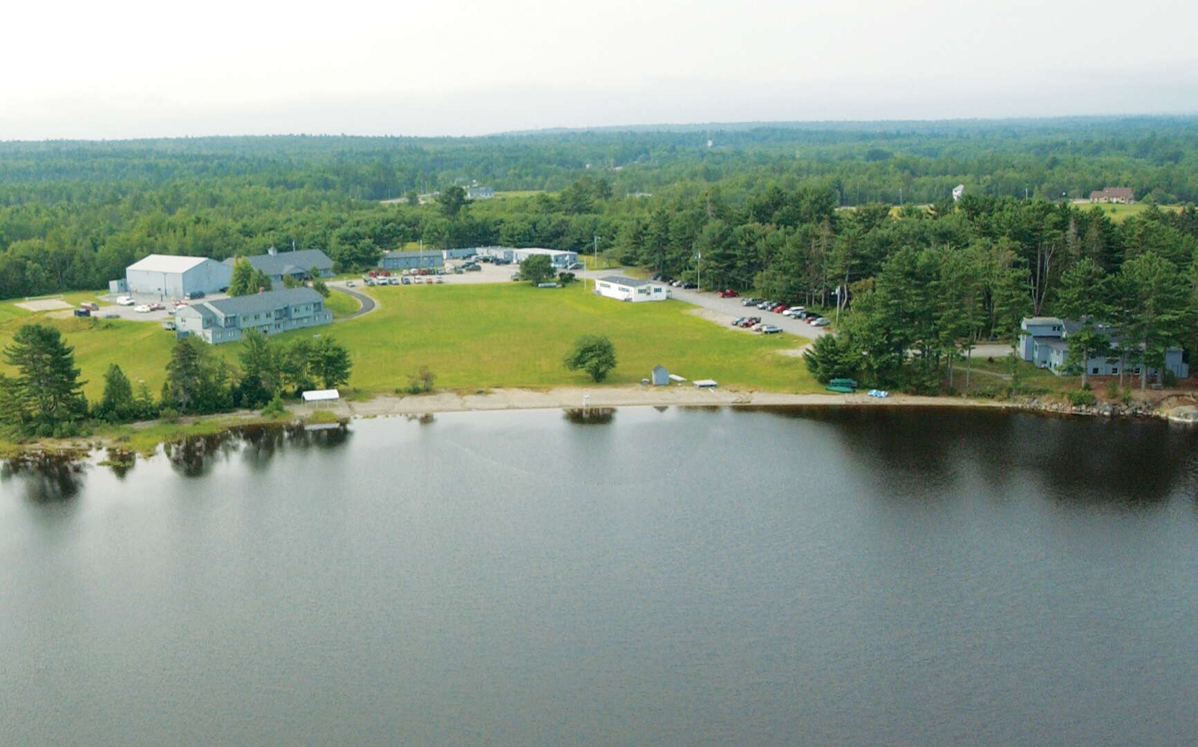 An aerial view shows water, lawns, buildings, and woods.