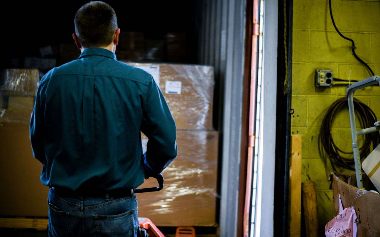 A person maneuvers a handcars with plastic-wrapped cartons.
