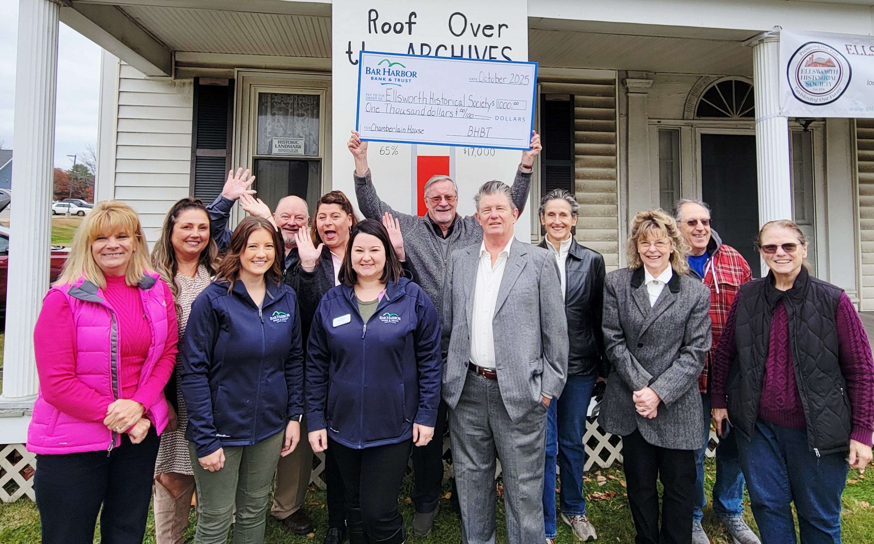 A group of people pose on a lawn in front of a porch.