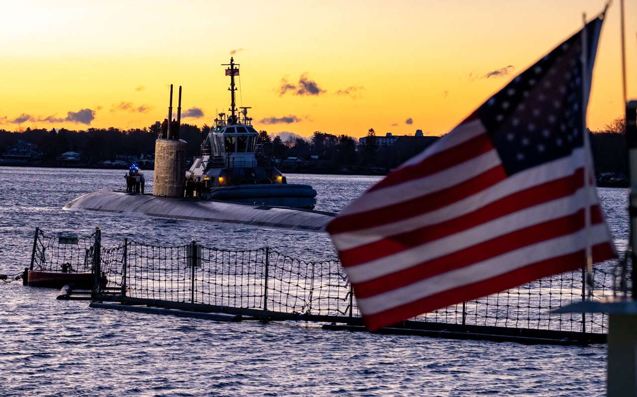 A flag flies in the foreground and a sub is in the water in the background.