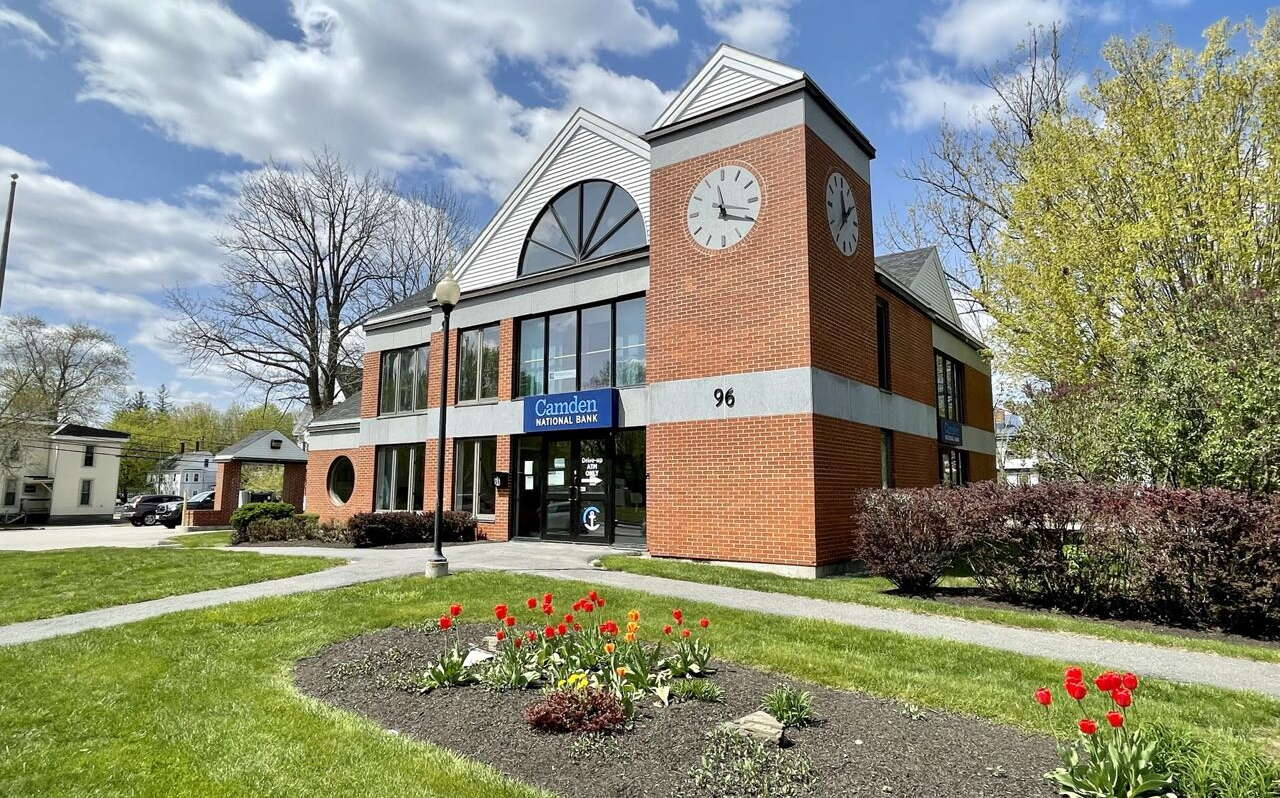 An exterior view of a brick building with tower and lawn.