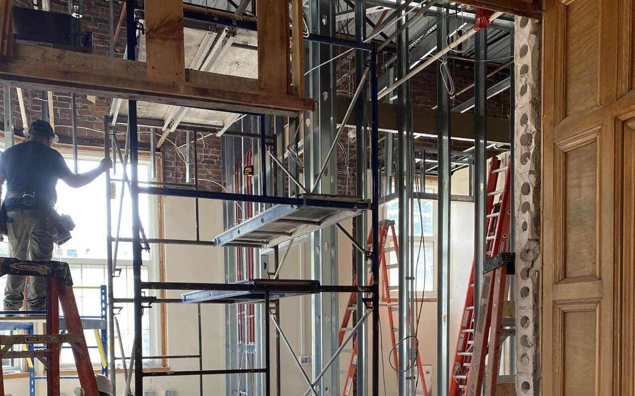 Scaffolding and a man on a ladder are inside a room.