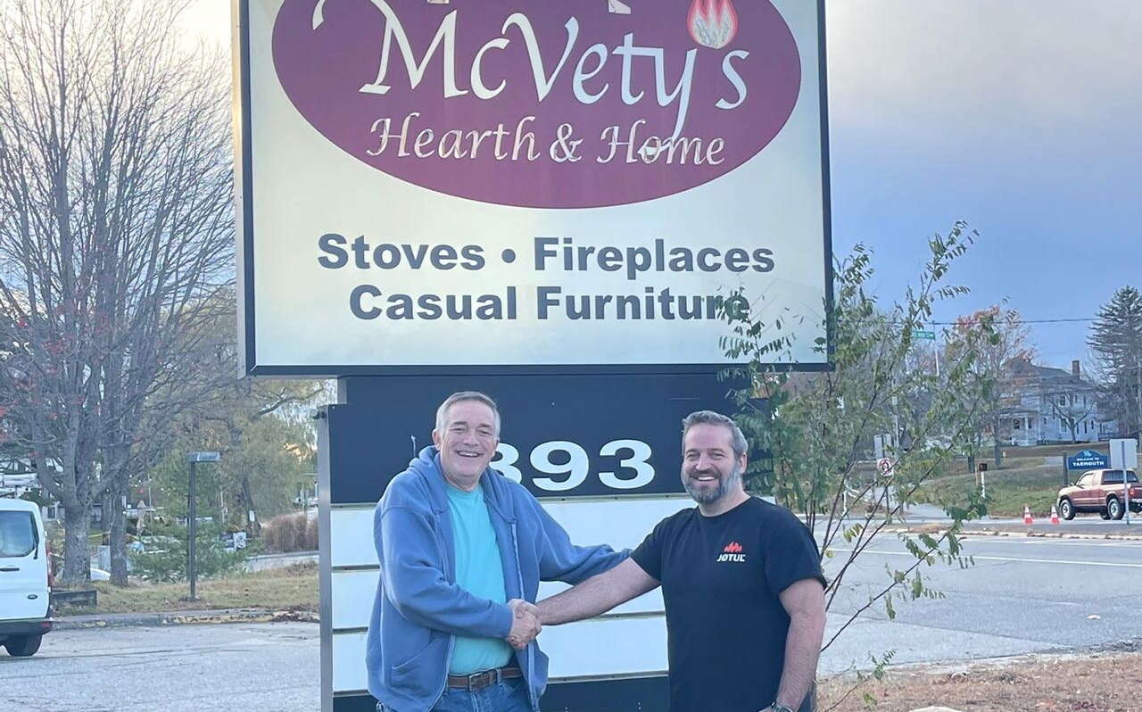 Two people shake hands in front of a sign.