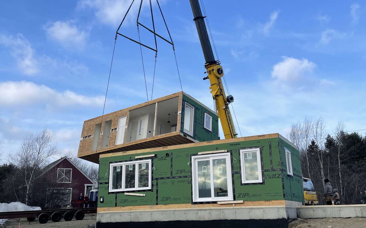 A crane lowers a wooden box onto another wooden box.