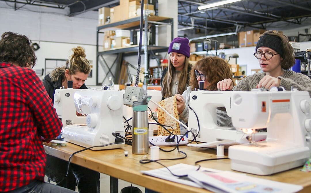 People sit in a large room at sewing machines.