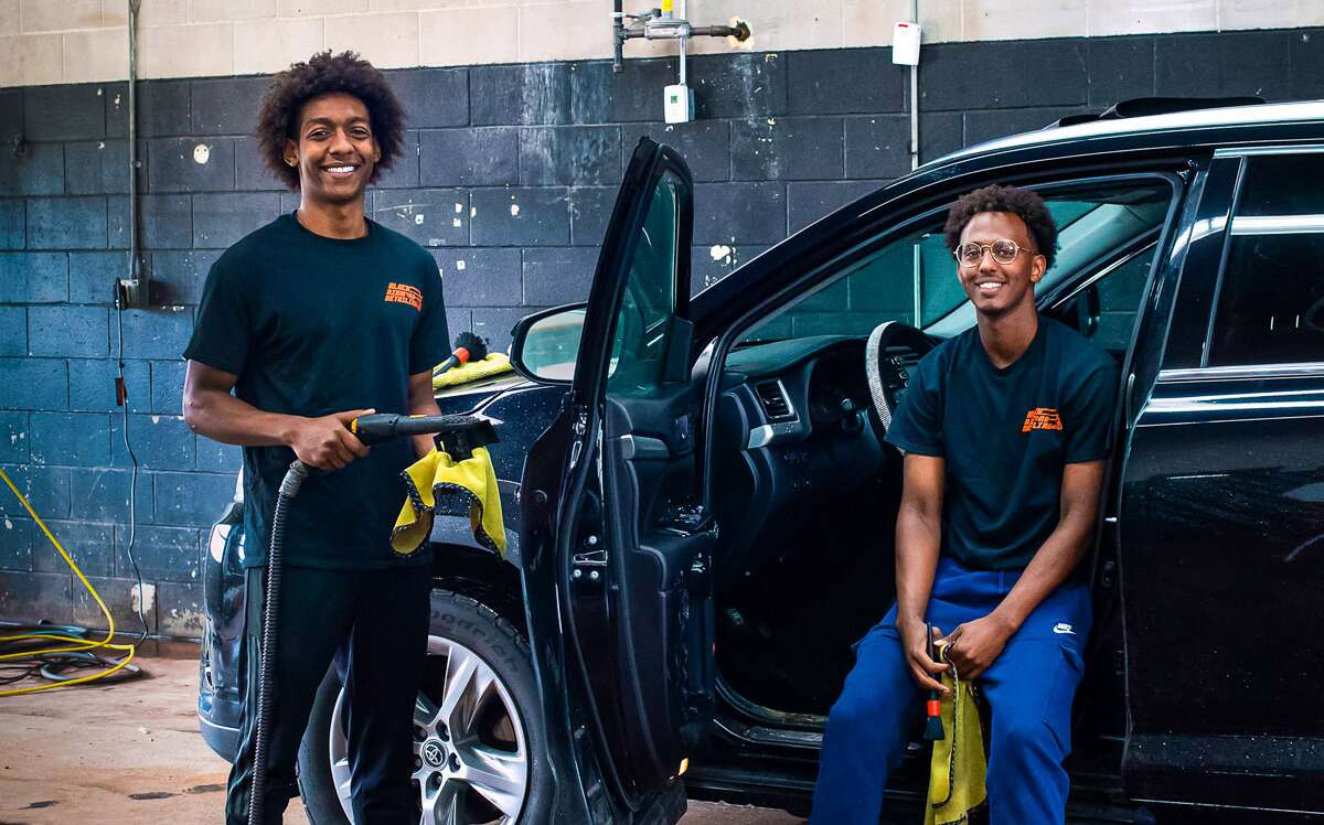 Owners of Black Diamond Detailing inside garage with car.