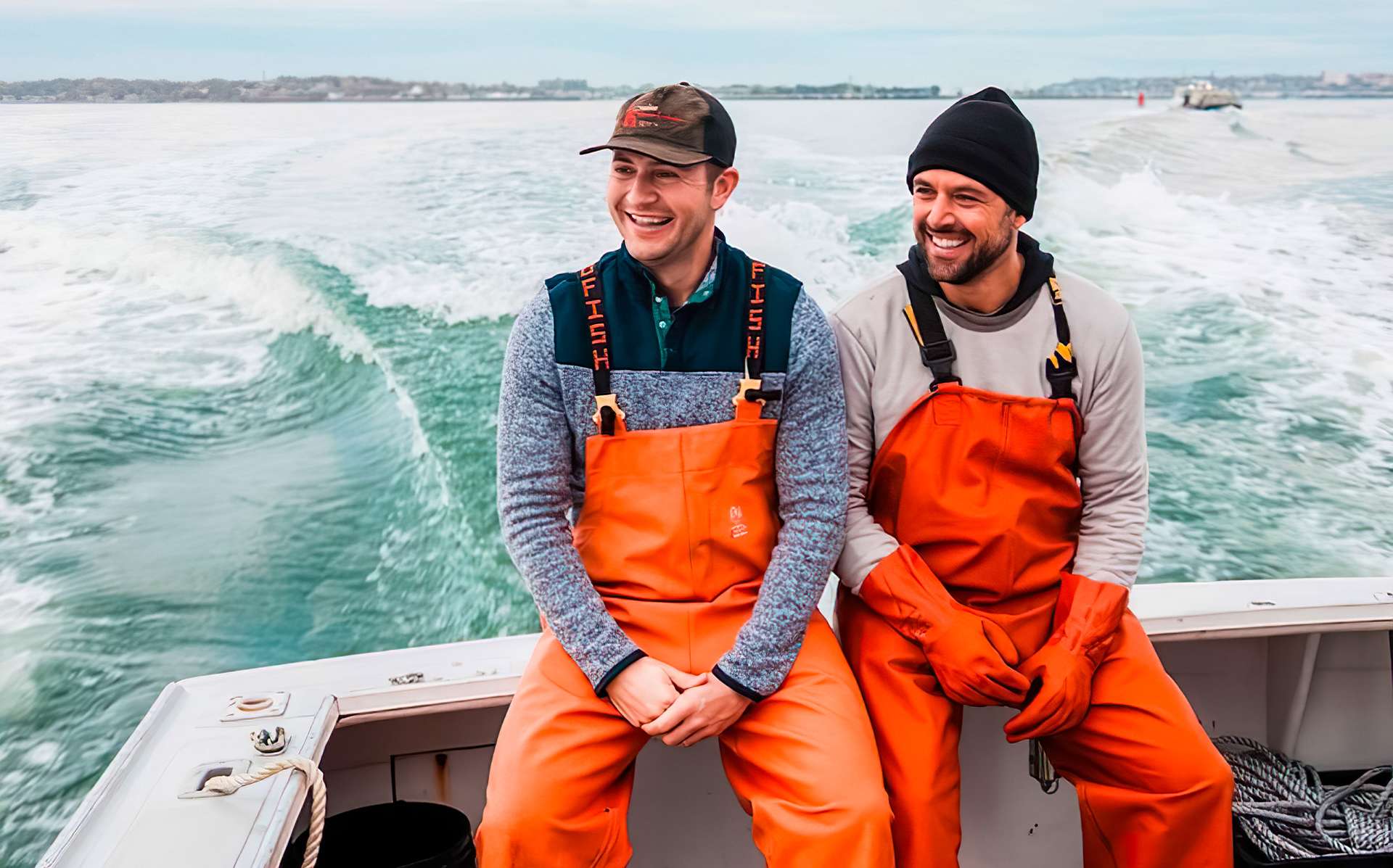 Jim and Sabin on a lobster boat on the water, they're clad in orange jumpsuits