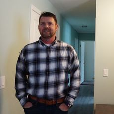 Man in flannel shirt and jeans standing in hallway of house