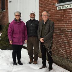 A woman and two men standing in the snow in front of a brick building that has a sign the brick house on it.
