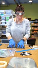 Flowfold worker wearing a protective face shield as she makes them. 