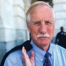 Sen. Angus King with white hair and a mustache portrait photo with a jacket over his shoulder 