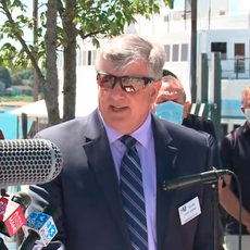 Steve Hewins at a press conference behind a bunch of TV microphones