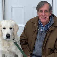 a smiling man sitting on steps outdoors next to a white labrador retriever