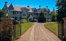 A very large three-story gray house with stone pillars and a gate
