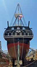 A view of the stern of the USS Constitution, a wooden ship with a high mast, sitting in dry dock