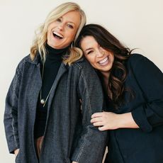 Two white women leaning on each other and laughing, one blond and one brunette