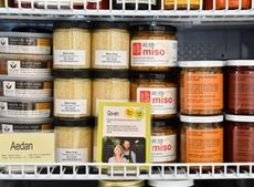 Small jars on a white wire shelf say Miso, mustard and other fermentation products