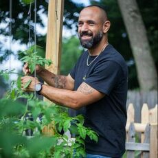 smiling man in black tee shirt next to garden plants