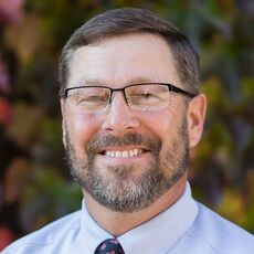 Bearded man in blue shirt and tie wearing glasses