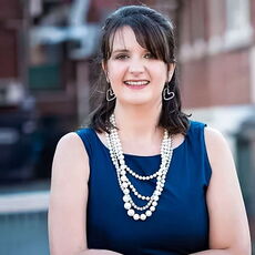 person smiling in blue sleeveless dress and faux pearl necklaces