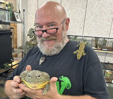 A person holds a frog and has a reptile on his shoulder.